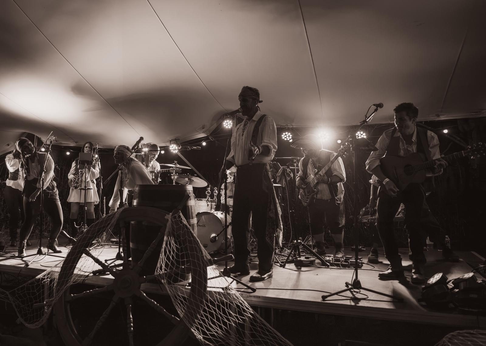 Wide view of the stage with the whole crew playing, nets and the ship’s wheel lit from above