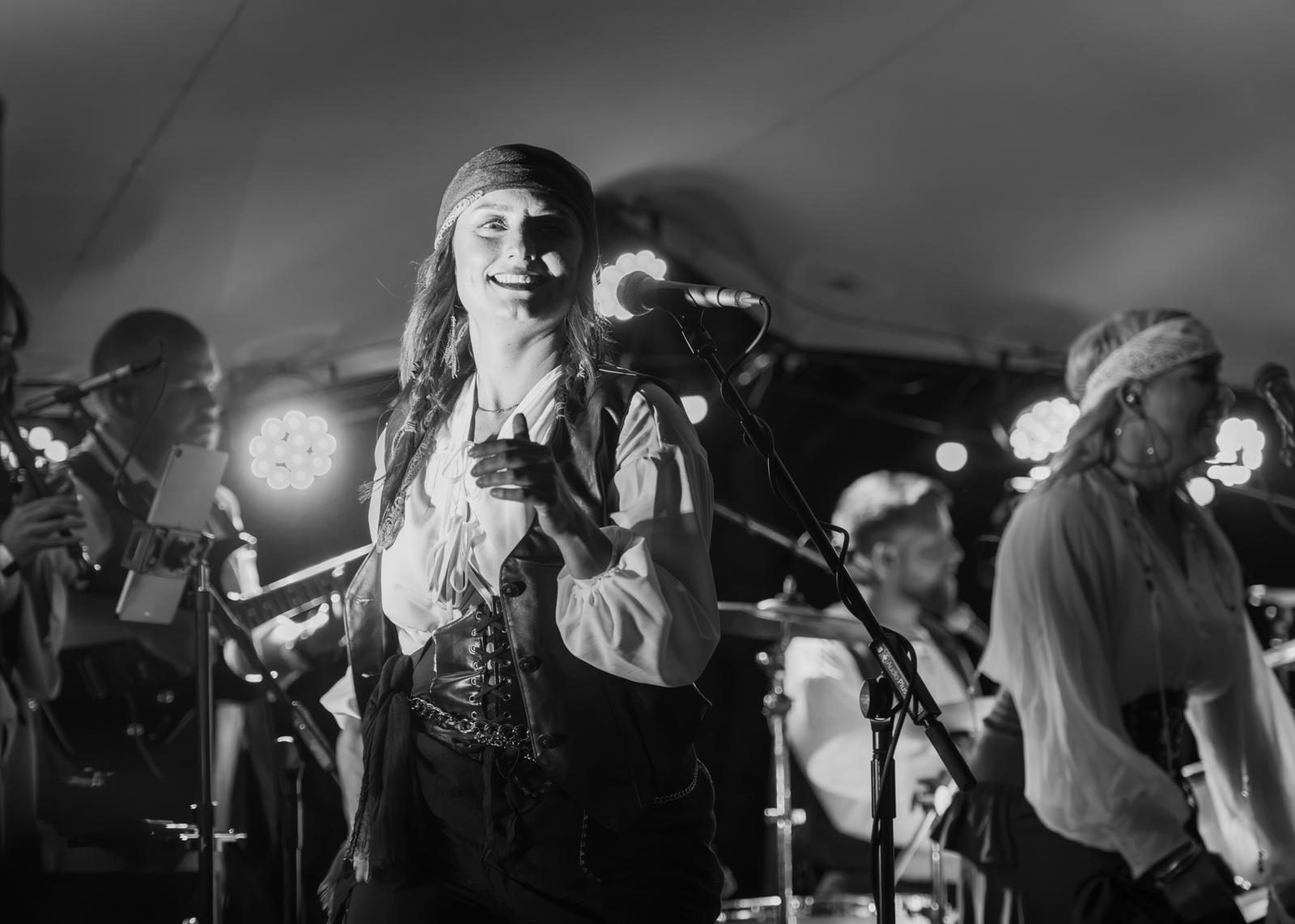 A singer in a waistcoat and bandana grinning at the microphone